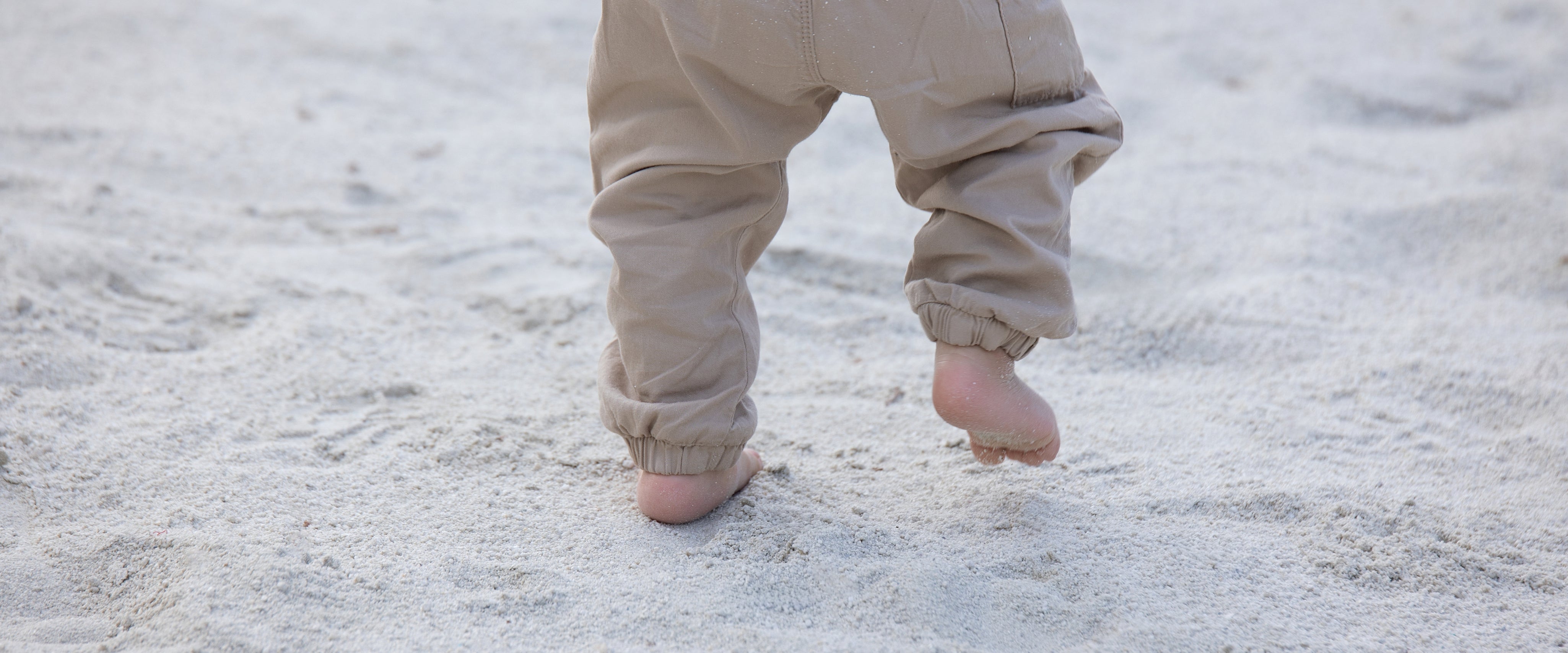 Pequeños pies descalzos de un niño caminando sobre la arena, símbolo de libertad y conexión natural que inspira el calzado respetuoso Gullibare.
