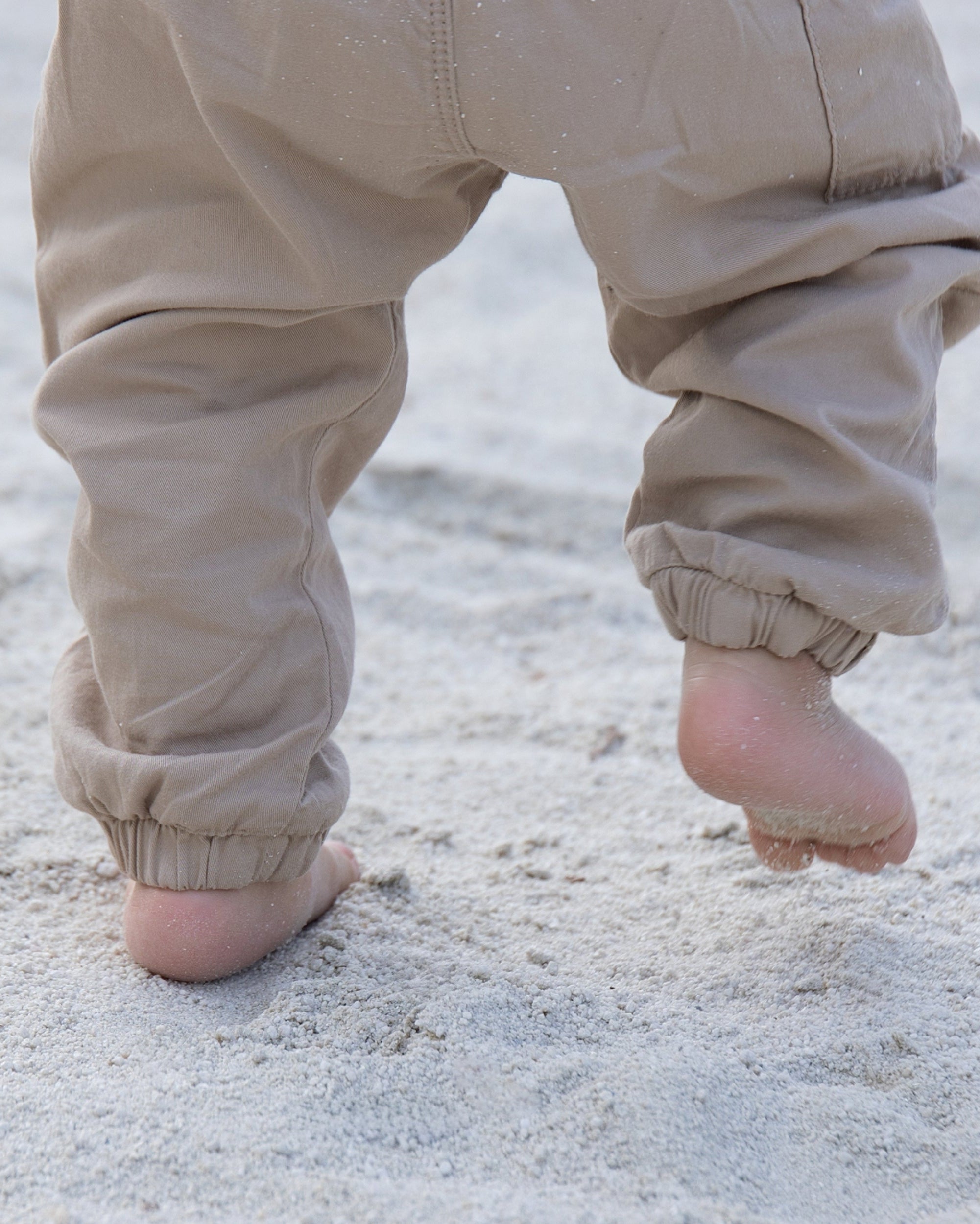 Pequeños pies descalzos de un niño caminando sobre la arena, símbolo de libertad y conexión natural que inspira el calzado respetuoso Gullibare.