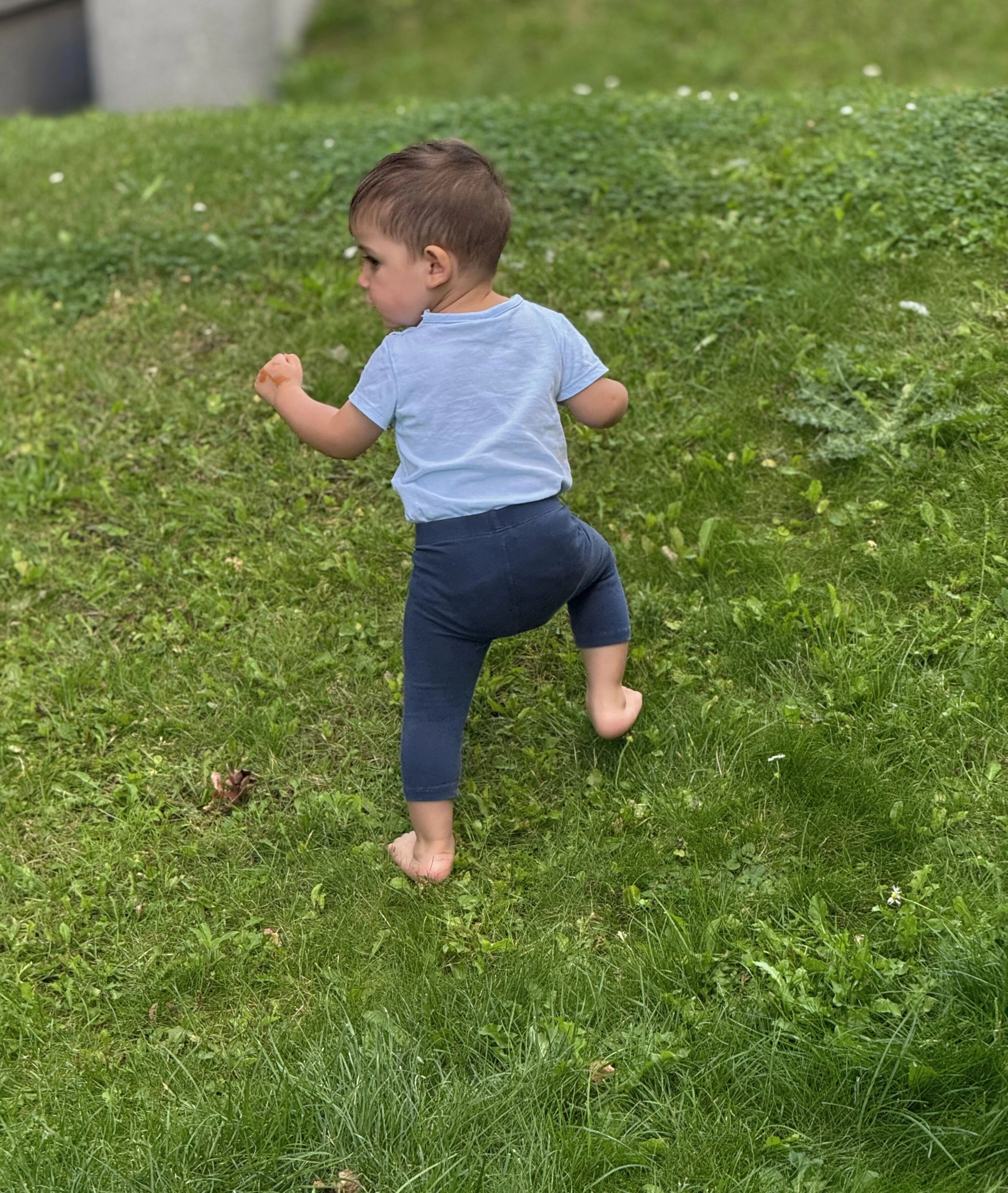 Bebé caminando descalzo sobre el césped, desarrollando el equilibrio y el movimiento natural en contacto directo con el suelo.