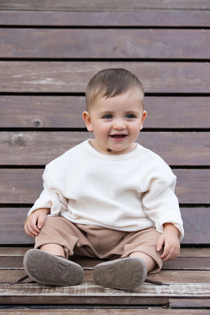 Bebé sentado de forma natural sobre escalones de madera, explorando el movimiento libre y la comodidad con calzado respetuoso Gullibare.