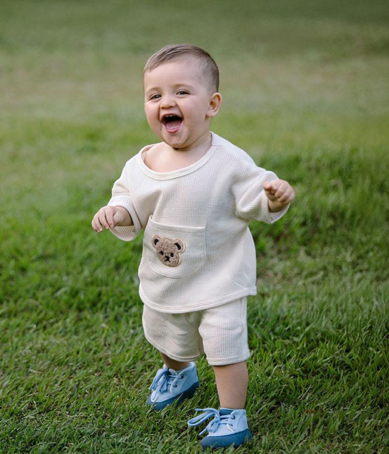 Bebé dando sus primeros pasos sobre el césped, usando calzado Gullibare azul, un calzado respetuoso, ligero y flexible que acompaña el movimiento natural del pie.