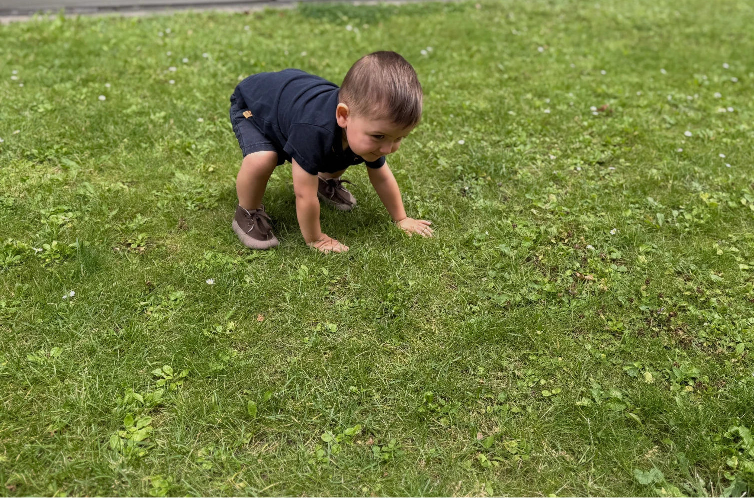 Bebé en sus primeras exploraciones sobre el césped, moviéndose con libertad y equilibrio mientras usa calzado respetuoso y flexible que acompaña el movimiento natural del pie.