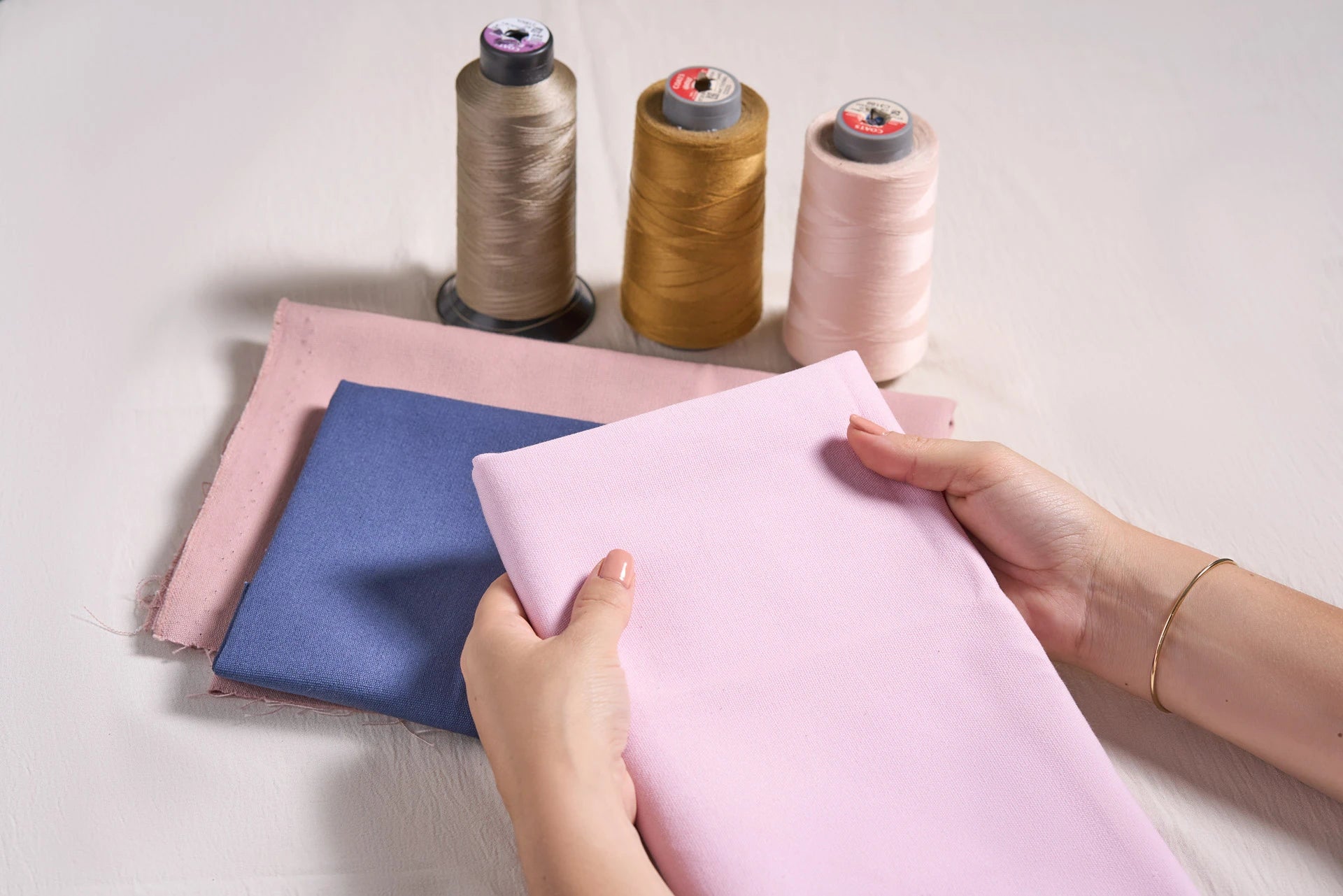 Tejidos de algodón orgánico en tonos rosa y azul junto a hilos naturales, materiales utilizados en la confección artesanal del calzado respetuoso Gullibare para bebé.