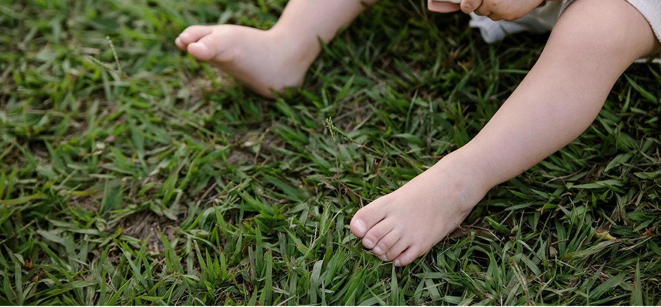 Bebé sentado sobre césped jugando con un juguete, mostrando movimiento natural del pie, en contexto de calzado respetuoso Gullibare.